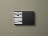 Black business card mockup on a grey paper stock background top view.